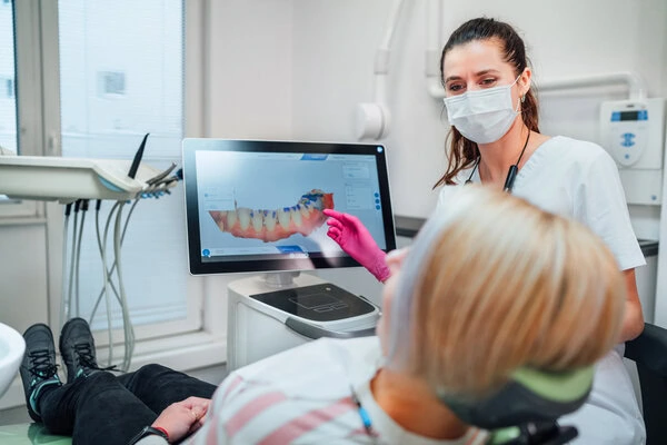 Dental professional in mask showing patient 3D scan of teeth on computer screen