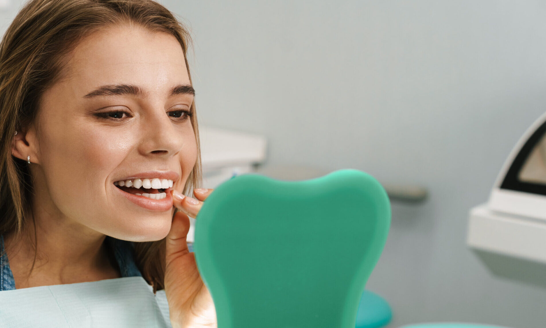 European young woman smiling while looking at mirror in dental clinic