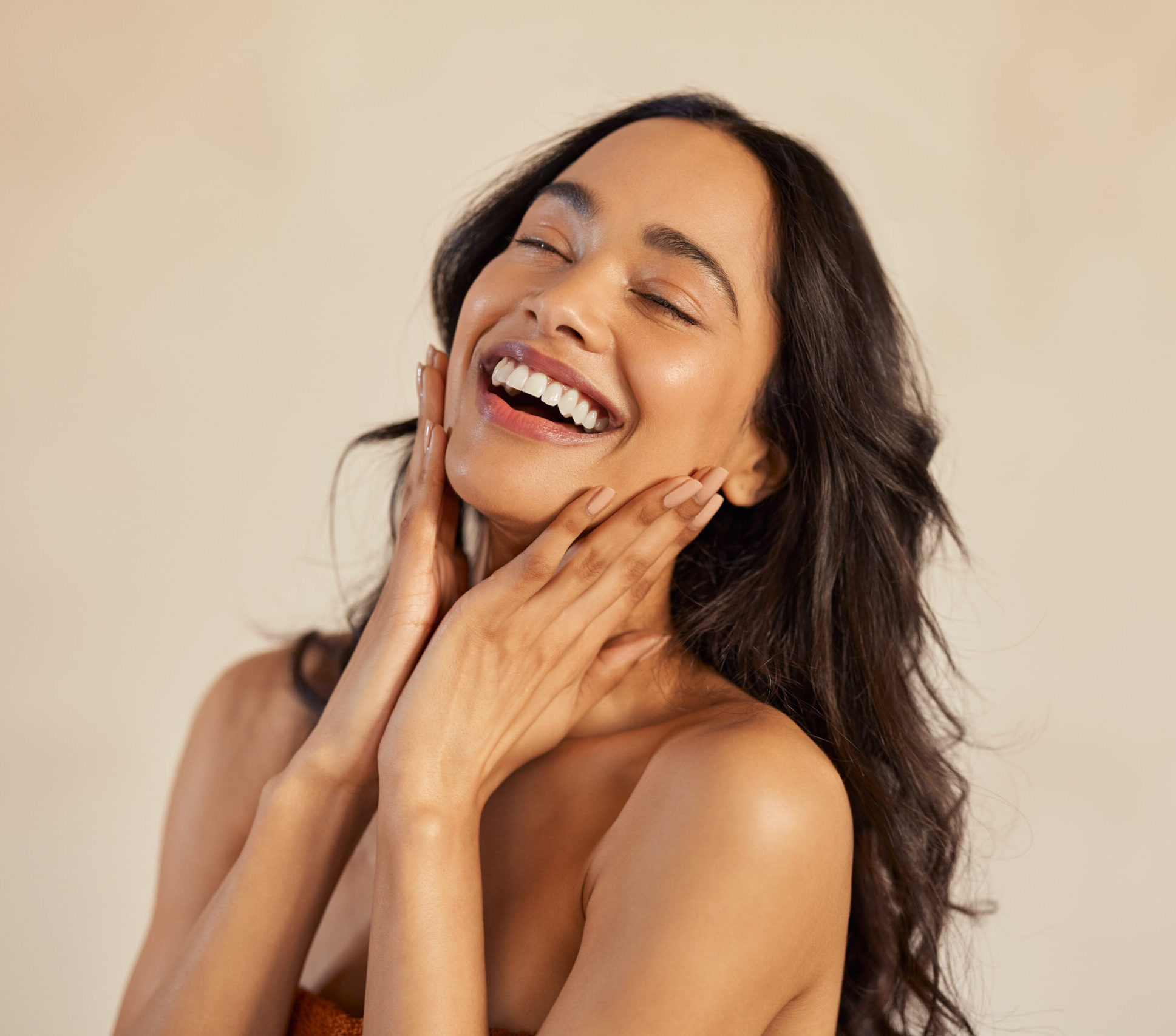 Multiethnic young woman touching her clean and healthy face against background with closed eyes. Latin hispanic woman feeling good with perfet skincare routine. Natural beauty portrait of mexican girl with black long hair.